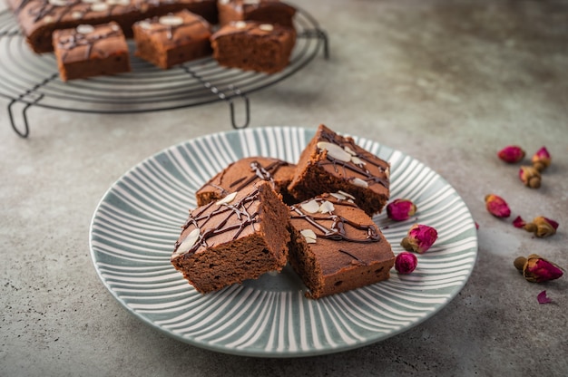 Hausgemachte Brownies mit Mandelblättern und Rosenknospen auf einem strukturierten Teller auf einem hölzernen Hintergrund.