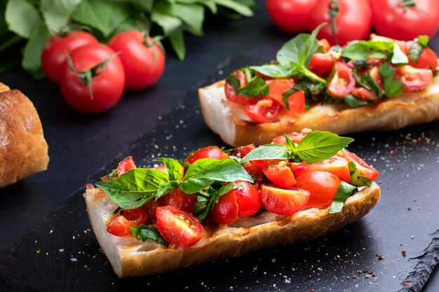 Hausgemachte Bruschetta mit Kirschtomaten und Basilikum Nahaufnahme auf einem Schieferbrett. Italienische Küche. Antipasti. Veganes Essen