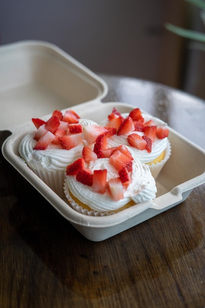 Foto hausgemachte buttercream-cupcakes mit frischen erdbeeren in einem take-away-container auf einem holztisch