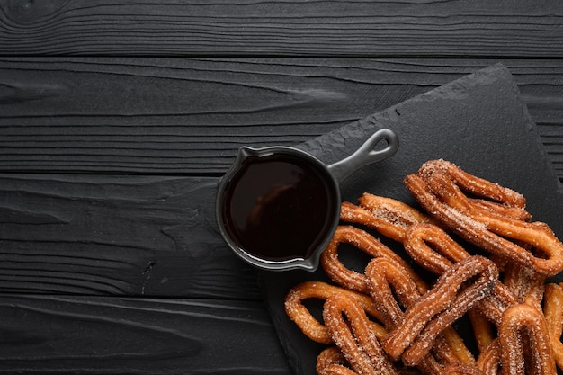 Hausgemachte Churros mit Schokolade auf dunklem rustikalem Holzhintergrund