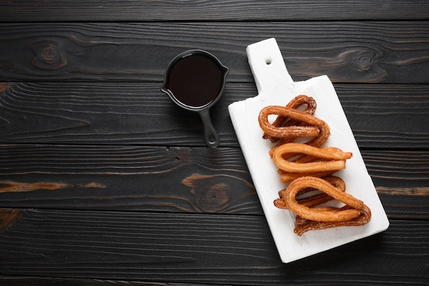 Hausgemachte Churros mit Schokolade auf dunklem rustikalem Holzhintergrund