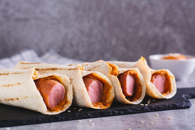 Hausgemachte Corn Dogs in gegrillter Tortilla mit Sauce auf Schiefer auf dem Tisch