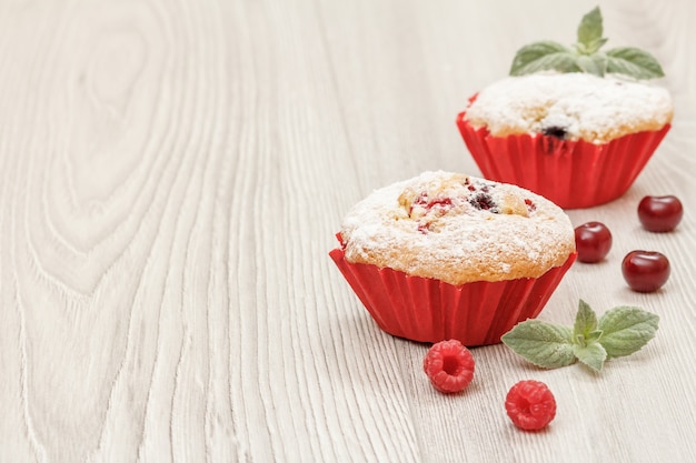 Hausgemachte Cupcakes bestreut mit Puderzucker und frischen Himbeeren, Minze auf Holzbrettern.