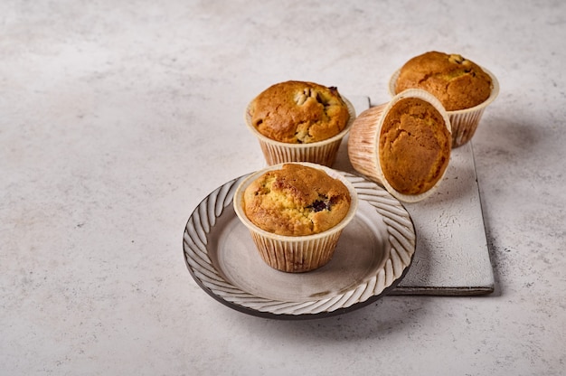 Hausgemachte Cupcakes in Backpapierformen auf Teller und zerkratztem Keramikschneidebrett auf Grau