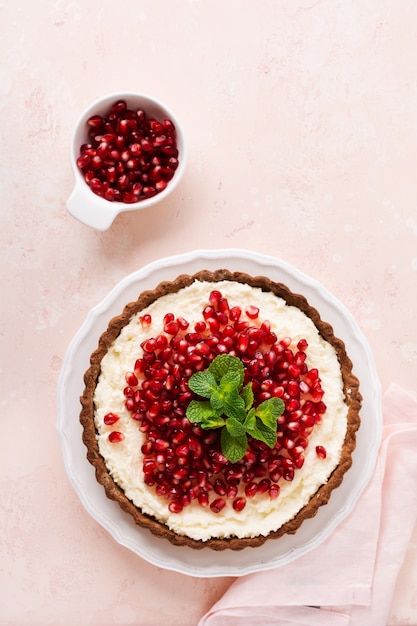 Hausgemachte Dessertschokoladentarte mit Kokoscreme und Granatapfel und Minze auf einer rosa Tischoberfläche. Draufsicht.