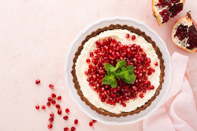 Hausgemachte Dessertschokoladentarte mit Kokoscreme und Granatapfel und Minze auf einer rosa Tischoberfläche