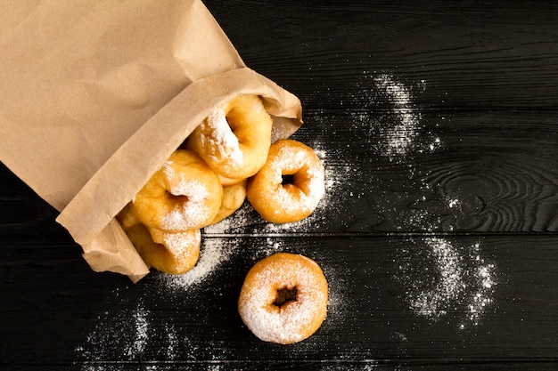 Hausgemachte Donuts mit Puderzucker in der Papierverpackung auf dem schwarzen hölzernen Hintergrund. Draufsicht. Speicherplatz kopieren.