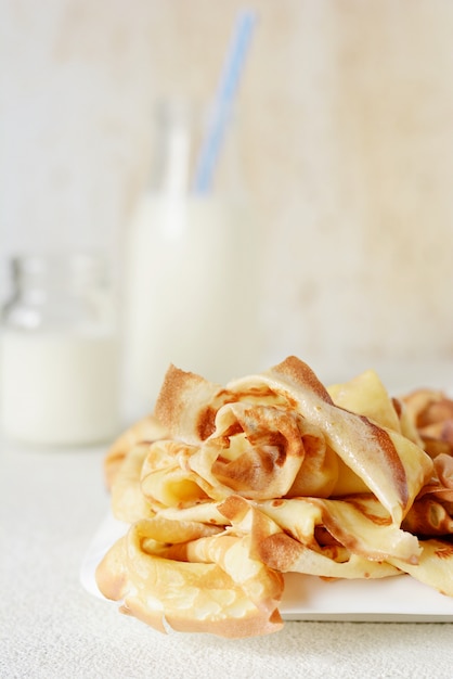 Hausgemachte dünne Pfannkuchen mit Beeren, Honig und Milch zum Frühstück auf hellem Hintergrund