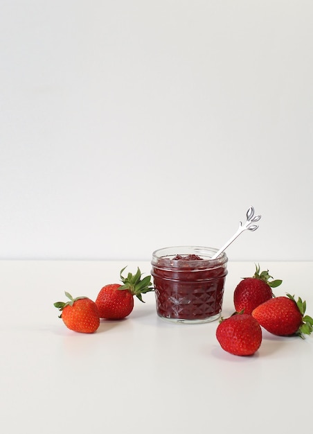 Hausgemachte Erdbeerkonserven oder Marmelade in einem Einmachglas, umgeben von frischen Bio-Erdbeeren Selektiver Fokus mit weißem Hintergrund