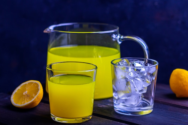 Hausgemachte erfrischende Zitruslimonade im Krug und im Glas und Glas mit Eiswürfeln auf einem hölzernen Hintergrund. Frischer Orangensaft. Das Konzept von Bio-Getränken und frischen Vitaminen