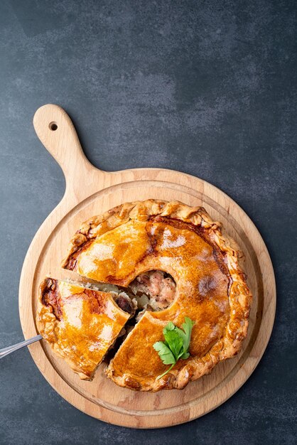 Hausgemachte Fleischpastete mit Grün auf Holzschneidebrett auf dunklem Tisch