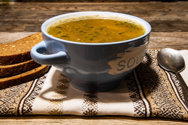 Foto hausgemachte fleischsuppe in einer blauen keramikschale, metalllöffel, folklorserviette auf einem holztisch.