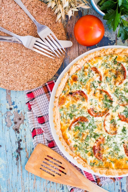 Hausgemachte französische Quiche-Torte mit Tomaten, Käse und Kräutern auf einem Teller auf einem Holztisch. Draufsicht