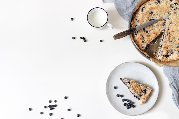 Hausgemachte frisch gebackene Heidelbeerkuchen Beeren Tasse Milch und Leinenserviette isoliert auf weißem Tischhintergrund Köstliches Fruchttortendessert Bäckereikonzept Flache Ansicht von oben