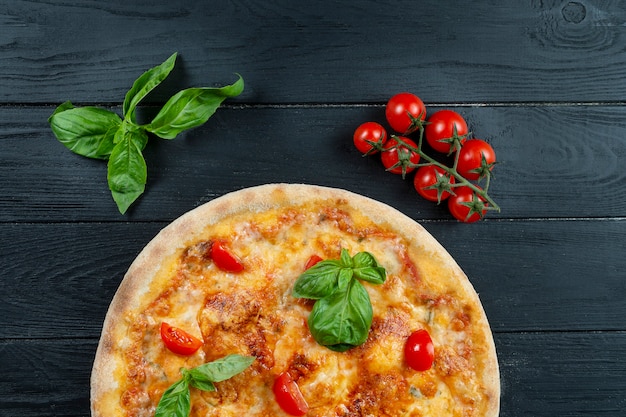 Hausgemachte frische Pizza Margherita mit roter Sauce, Basilikum und Kirschtomate auf einem schwarzen Holz mit Kopienraum.