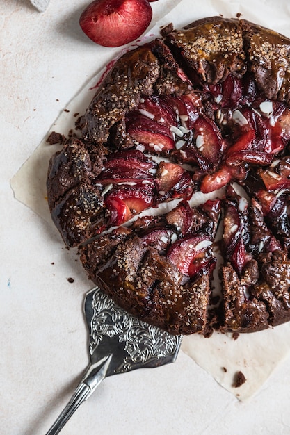 Hausgemachte Galette oder offene Torte mit Schokolade, Pflaume und Mandel auf hellem Hintergrund. Ansicht von oben.