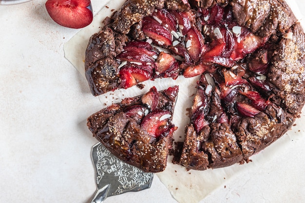 Hausgemachte Galette oder offene Torte mit Schokolade, Pflaume und Mandel auf hellem Hintergrund. Ansicht von oben.