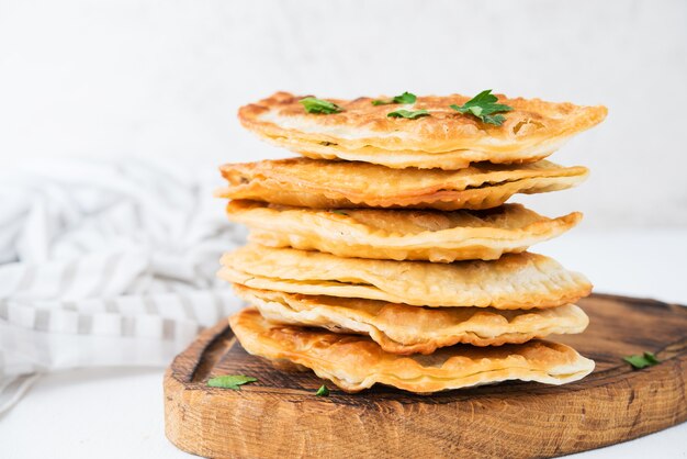 Hausgemachte gebratene Empanadas mit Schweinefleisch, Chebureks mit Pilzen auf einem Holzbrett, Nahaufnahme