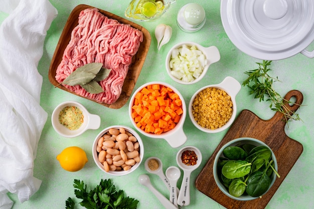 Hausgemachte Gemüsesuppe mit Fleischbällen und Spinat in einem weißen Topf auf grünem Hintergrund