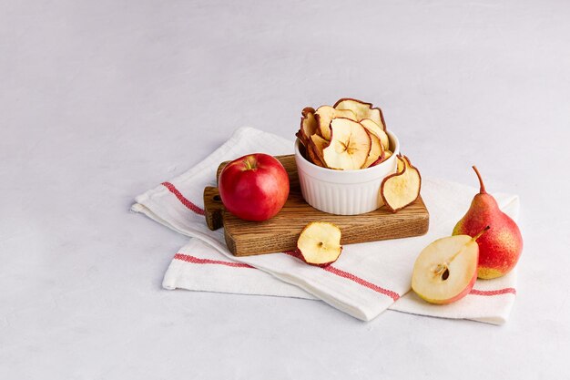 Hausgemachte getrocknete Apfel- und Birnenscheiben in einer Schüssel auf hellgrauem Hintergrund. Fruchtchips, veganes Dessert ohne Zucker