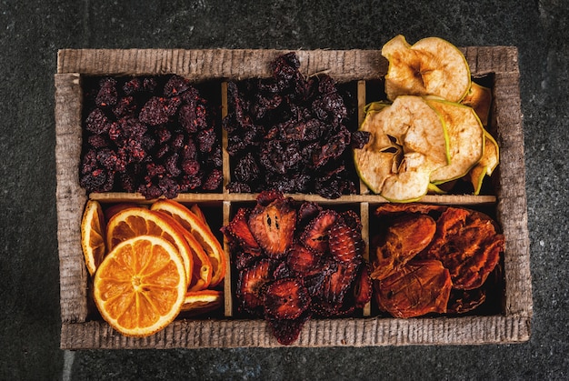 Hausgemachte getrocknete Beeren und Früchte, Ernte für den Winter: Aprikosen, Äpfel, Erdbeeren, Himbeeren, Kirschen, Orangen. In der alten Holzkiste auf schwarzer Steintischplatteansicht