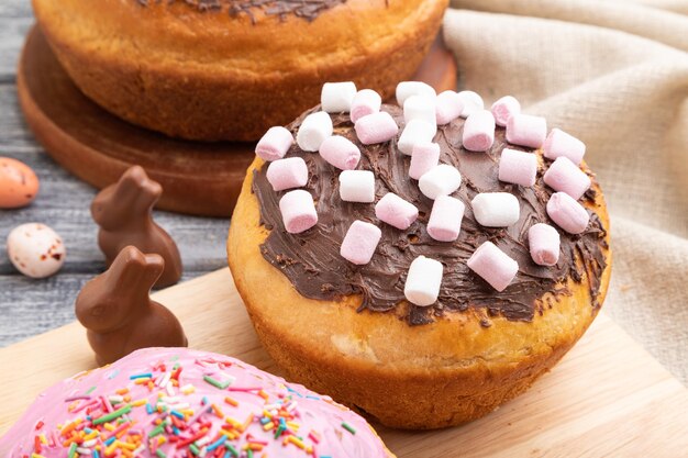 Hausgemachte glasierte und dekorierte Osterkuchen mit Schokoladeneiern und Kaninchen auf grauem Holzhintergrund und Leinengewebe. Seitenansicht, Nahaufnahme.