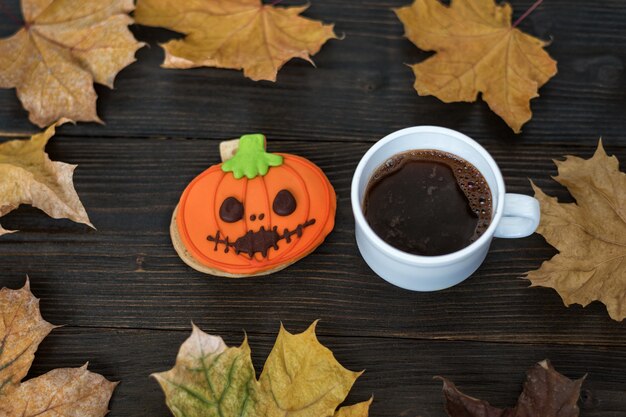 Hausgemachte Halloween Cookies Kürbis und Tasse Kaffee auf Holztisch mit Herbstlaub.