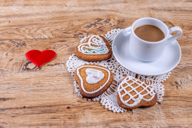 Hausgemachte herzförmige Kekse mit weißem Zuckerguss und Streuseln mit Kaffee