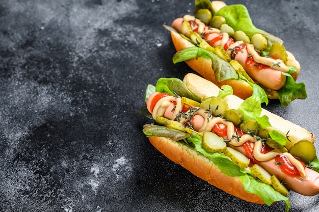 Hausgemachte Hot Dogs mit Gemüse, Salat und Gewürzen. Schwarzer Hintergrund. Draufsicht. Speicherplatz kopieren.