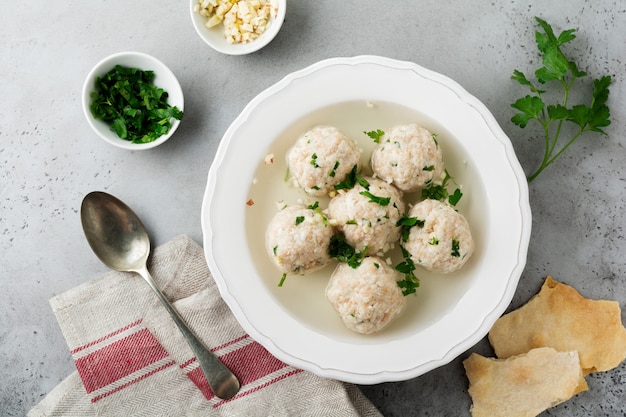 Hausgemachte Hühnermatzo-Ballsuppe mit Petersilie und Knoblauch in einfacher weißer Keramikplatte auf einem grauen Stein oder Beton