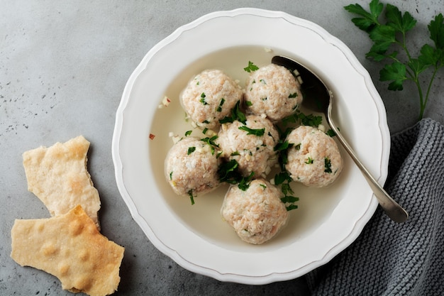 Hausgemachte Hühnermatzo-Ballsuppe mit Petersilie und Knoblauch in einfacher weißer Keramikplatte auf einem grauen Stein oder Beton