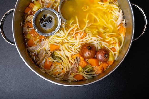 Hausgemachte Hühnersuppe mit Nudeln und Gemüse in Metallpfanne auf schwarzem Tisch Draufsicht