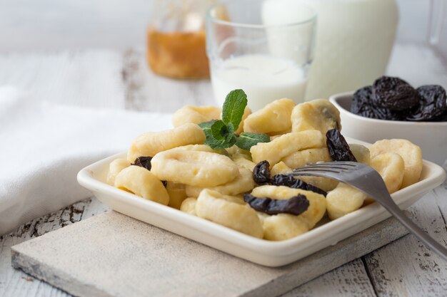 Hausgemachte Hüttenkäse-Gnocchi (faule Knödel) mit Vanillesauce und Minze in einer weißen Schüssel, selektiver Fokus.