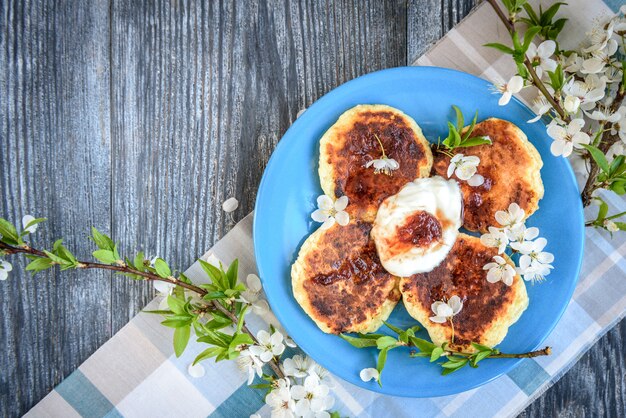 Hausgemachte Hüttenkäsepfannkuchen auf blauem Teller mit Frühlingskirschpflaumenzweigen auf hölzernem Hintergrund.