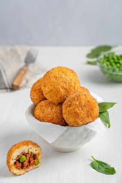 Hausgemachte italienische oder sizilianische Arancini-Reisbällchen, gefüllt mit Hackfleisch und grünen Erbsen in einer Schüssel auf dem Tisch