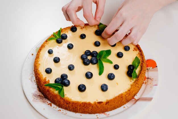 Hausgemachte Käsekuchenhanddekoration mit Blaubeerbeeren und Minzblättern. Kochen von Desserts und Kuchen. Süßwaren.