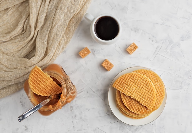 Hausgemachte Karamellsauce in einem Glas auf einem Leuchttisch. Espresso in einer weißen Tasse und frischen Waffeln. Draufsicht Süßes Dessert.