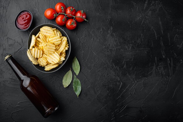 Hausgemachte Kartoffelchips mit Flasche Bier auf schwarzem Stein, Draufsicht flach gelegt