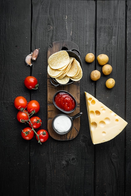 Hausgemachte Kartoffelchips mit Käse und Zwiebeln, auf schwarzem Holztisch, Draufsicht flach gelegt