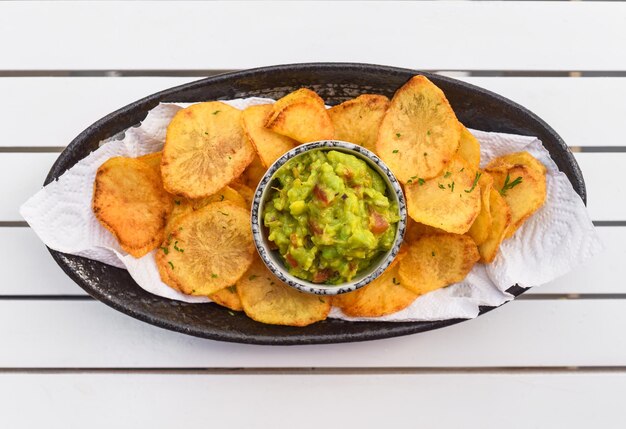 Hausgemachte Kartoffelchips mit vegetarischer Sauce aus Avocado und Gemüse auf weißem Holztisch