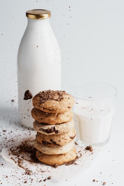 Hausgemachte Kekse, auf denen zerkleinerte Schokolade auf dem Hintergrund einer Flasche und eines Glases Milch bestreut wird