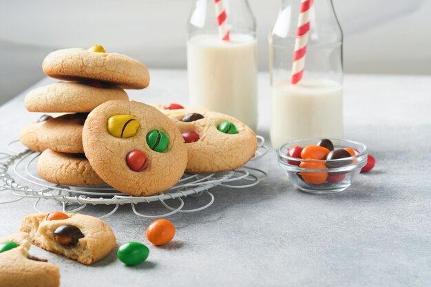 Hausgemachte Kekse mit bunten Pralinen und Milch Stack of Shortbread Cookies mit mehrfarbigen Süßigkeiten auf Teller mit Flasche Milch auf hellgrauem Hintergrund Babynahrungskonzept Kopieren Sie Platz