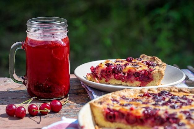 Foto hausgemachte kirschkuchenkuchen und roter kirschgetränk auf dem holztisch im gartenhintergrund