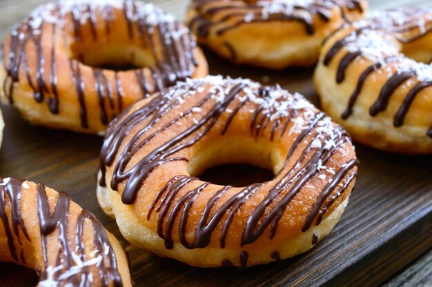 Hausgemachte klassische Donuts mit Schokolade und Kokosflocken auf dunklem Holzhintergrund. Nahansicht.