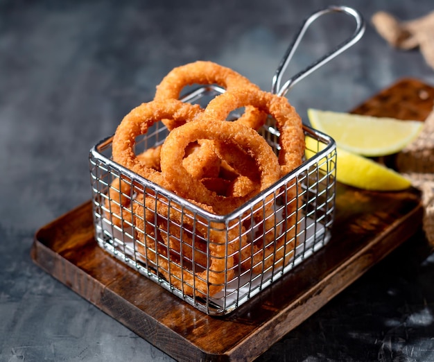 Hausgemachte knusprig gebratene Zwiebelringe in einer Friteuse mit Limettendraufsicht auf dunklem Hintergrund