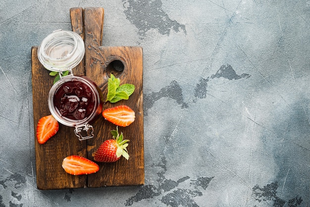 Hausgemachte köstliche Erdbeermarmelade und mit frischen Beeren, auf grauem Hintergrund, Draufsicht flach lag mit Kopierraum für Text