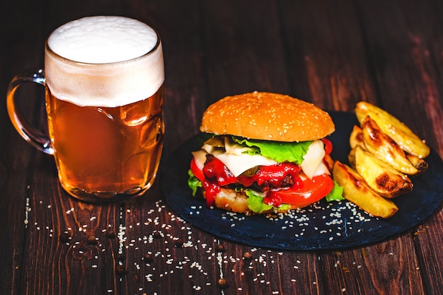 Hausgemachte köstliche, leckere Beef Burger mit Salat und Kartoffeln, ein Glas Bier serviert auf Stein Schneidebrett. Dunkel