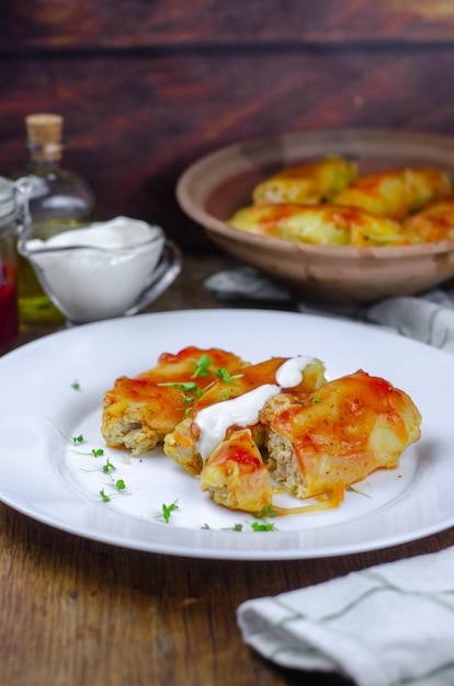 Hausgemachte Kohlrouladen mit Karotten, roter Tomatensauce und Sahne auf einem weißen Teller