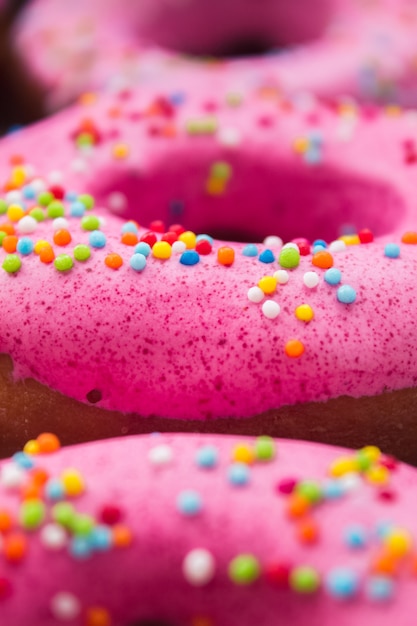 Hausgemachte Kreiskrapfen mit rosa Zuckerguss und Regenbogenstreuseln in weißer Box auf Bastelpapier.