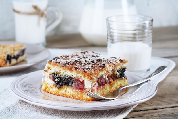 Hausgemachte Kuchen mit Marmelade und Glas Milch auf Holztisch und hellem Stoffhintergrund